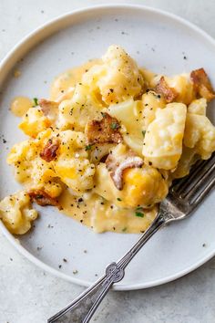 a white plate topped with macaroni and cheese on top of a table next to a fork