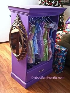 a purple cabinet with clothes hanging from it's sides and a mirror on top