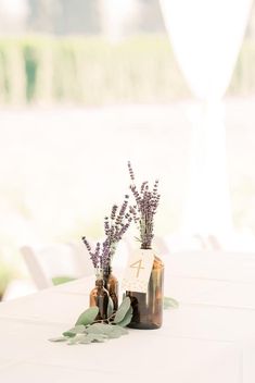 two vases filled with lavender flowers sitting on top of a white table covered in greenery