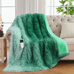 a couch with a green blanket on top of it next to a table and lamp