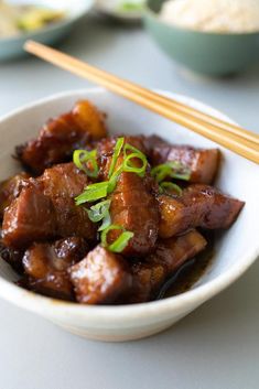 a white bowl filled with meat and chopsticks