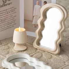 a white candle sitting next to a mirror on top of a carpeted floor in front of a magazine