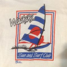 a white shirt with a blue and red sailboat on it's front, which reads waiki surf and surf club