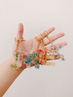 a person's hand holding several different types of bracelets on their fingers, with one being held in the air