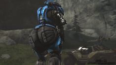 a blue and black robot standing in front of a mountain with an armored vehicle behind it