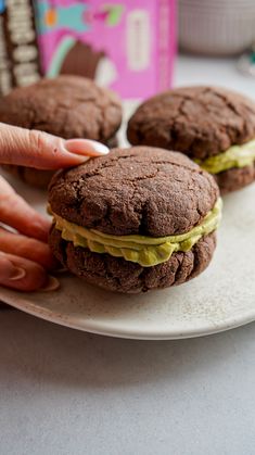 there is a person that is holding a chocolate sandwich on a plate with other cookies in the background