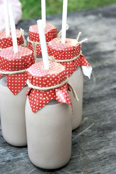 four jars with candles in them are sitting on a table outside and one has a red polka dot bow around the top