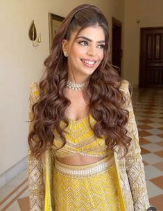 a woman with long brown hair wearing a yellow outfit and smiling at the camera while standing in a hallway