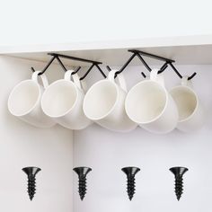 coffee cups are hanging on the wall with black screws in front of white walls