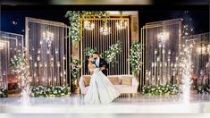 a bride and groom are sitting on a couch in front of a stage with chandeliers