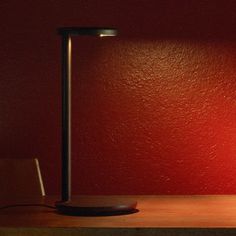 a table lamp sitting on top of a wooden desk next to a red painted wall