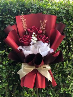 a bouquet of red roses and white flowers on top of a green bush in front of some bushes