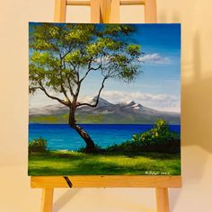 an easel with a painting on it and a tree in front of the water