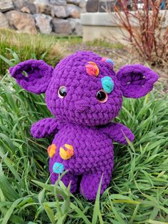 a purple crocheted elephant sitting in the grass with flowers on it's ears