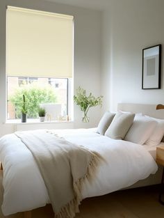 a white bed sitting under a window next to a wooden table with a potted plant on it