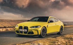 a yellow sports car is driving down the road with dark clouds in the sky behind it