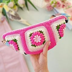 a hand holding a pink and white crocheted purse with flowers on the front