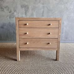 a small wooden chest of drawers sitting on top of a carpeted floor next to a wall