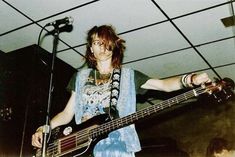 a woman standing in front of a microphone and holding a bass guitar while wearing a blue dress