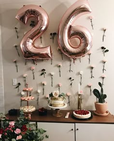 a table topped with balloons and flowers next to a wall covered in pink foil numbers