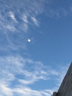 the moon is visible in the blue sky above a brick wall and clock tower on a sunny day