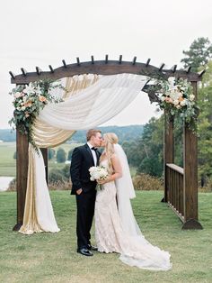 a bride and groom kissing under an outdoor wedding ceremony chute with flowers in the foreground