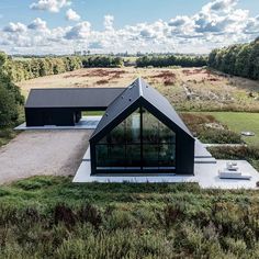 an aerial view of a black house in the middle of a field with trees and grass