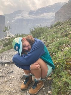 a woman is sitting on the side of a mountain with her head in her hands