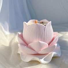 a pink flower sitting on top of a white cloth covered tablecloth with light coming through the petals