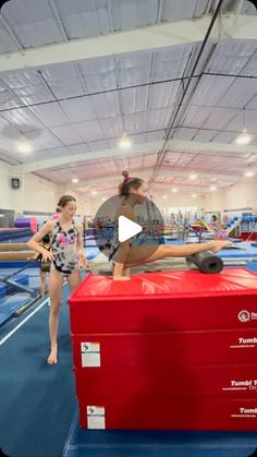 a woman standing on top of a red box in an indoor gymnastics court with another person behind her