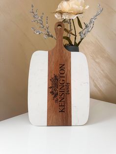 a wooden cutting board sitting on top of a table next to a vase with flowers