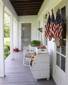 an american flag hanging on the front porch of a house with white siding and wood flooring