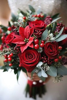 a bride holding a bouquet of red roses and greenery with berries on the stems