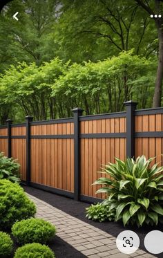 a wooden fence surrounded by lush green trees and shrubbery in front of a brick walkway