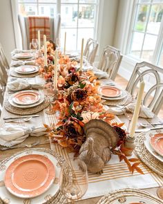 a table set for thanksgiving dinner with plates and place settings in front of large windows