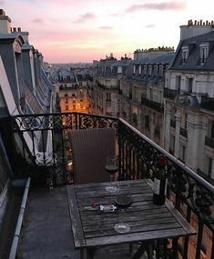 an outdoor table and chairs on a balcony overlooking the city at sunset or dawn with wine bottles, glasses and empty plates