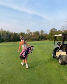 a man walking across a lush green field next to a golf cart with a bag on it