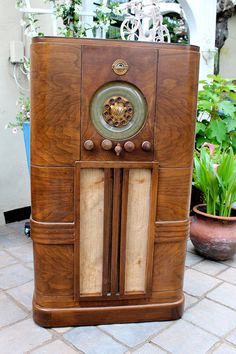 an old wooden radio sitting on top of a brick floor next to potted plants