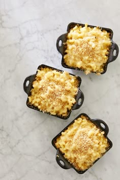 three small square dishes filled with macaroni and cheese on a marble countertop