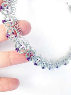 a hand is holding a silver and purple necklace