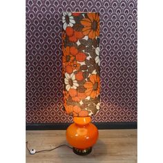 an orange vase sitting on top of a wooden table next to a wallpapered wall