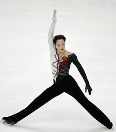 a male figure skating on the ice in a black and white outfit with red accents