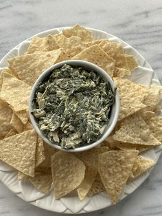 a white plate topped with tortilla chips next to a bowl of spinach