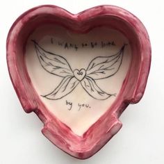 a pink heart shaped bowl with writing on the side and wings in the shape of a heart