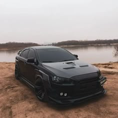 a black car parked on the side of a dirt road next to a body of water