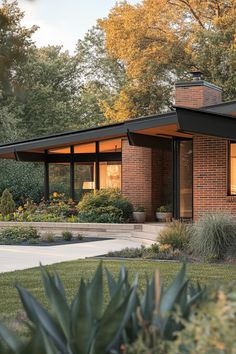 a brick house with large windows and plants in the front yard, surrounded by trees