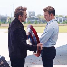 two men standing next to each other with captain america shield on their hands and one man holding the shield