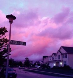 a street sign sitting on the side of a road under a pink sky with clouds