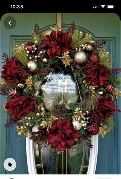 a christmas wreath with red flowers and greenery hangs on the front door's green door