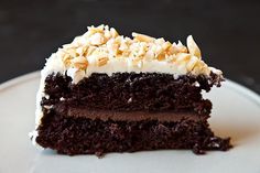 a piece of chocolate cake with white frosting and nuts on top sits on a plate